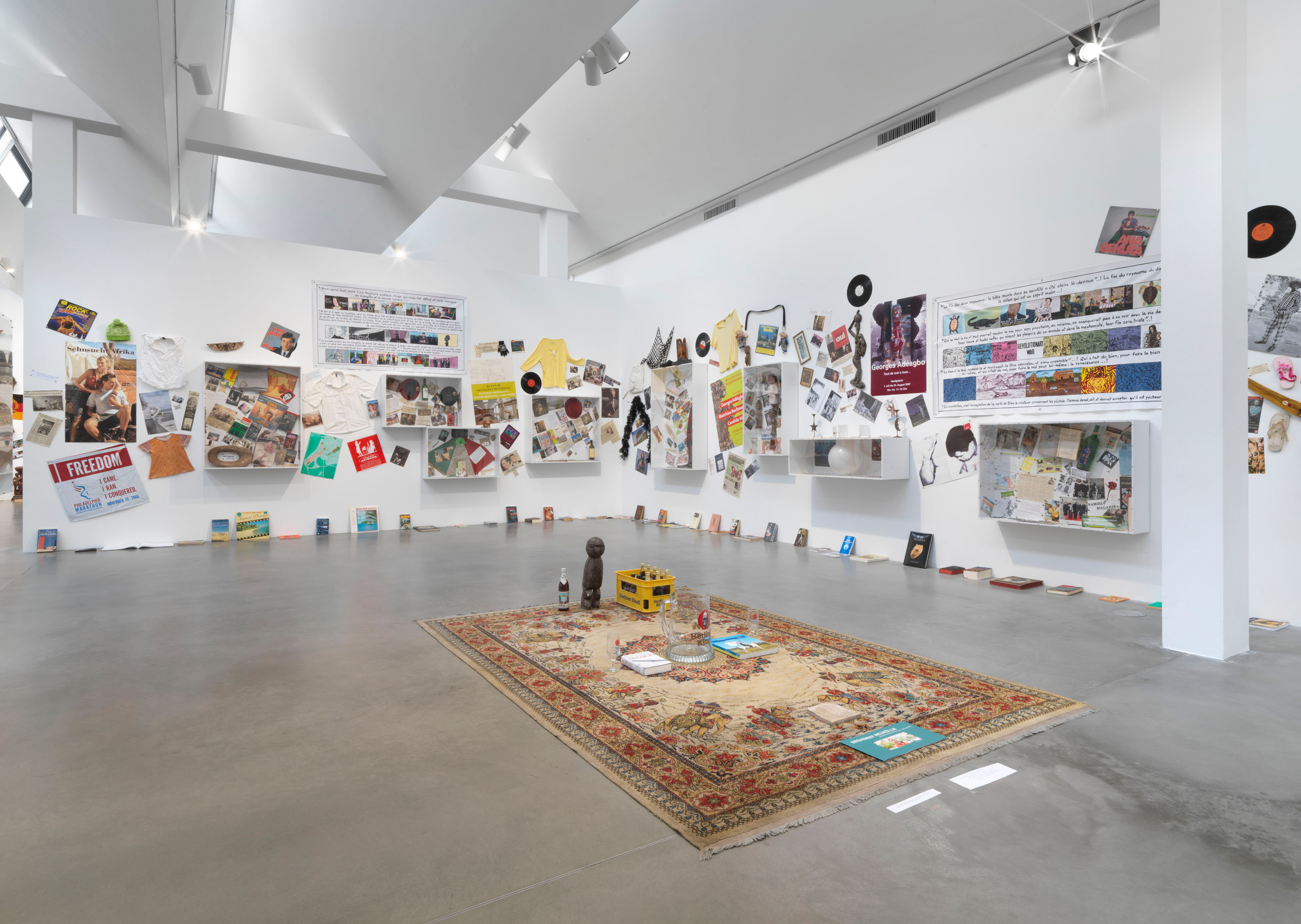 a large space with a persian carpet in the center, on the walls vitrines with objects, textiles, records and posters