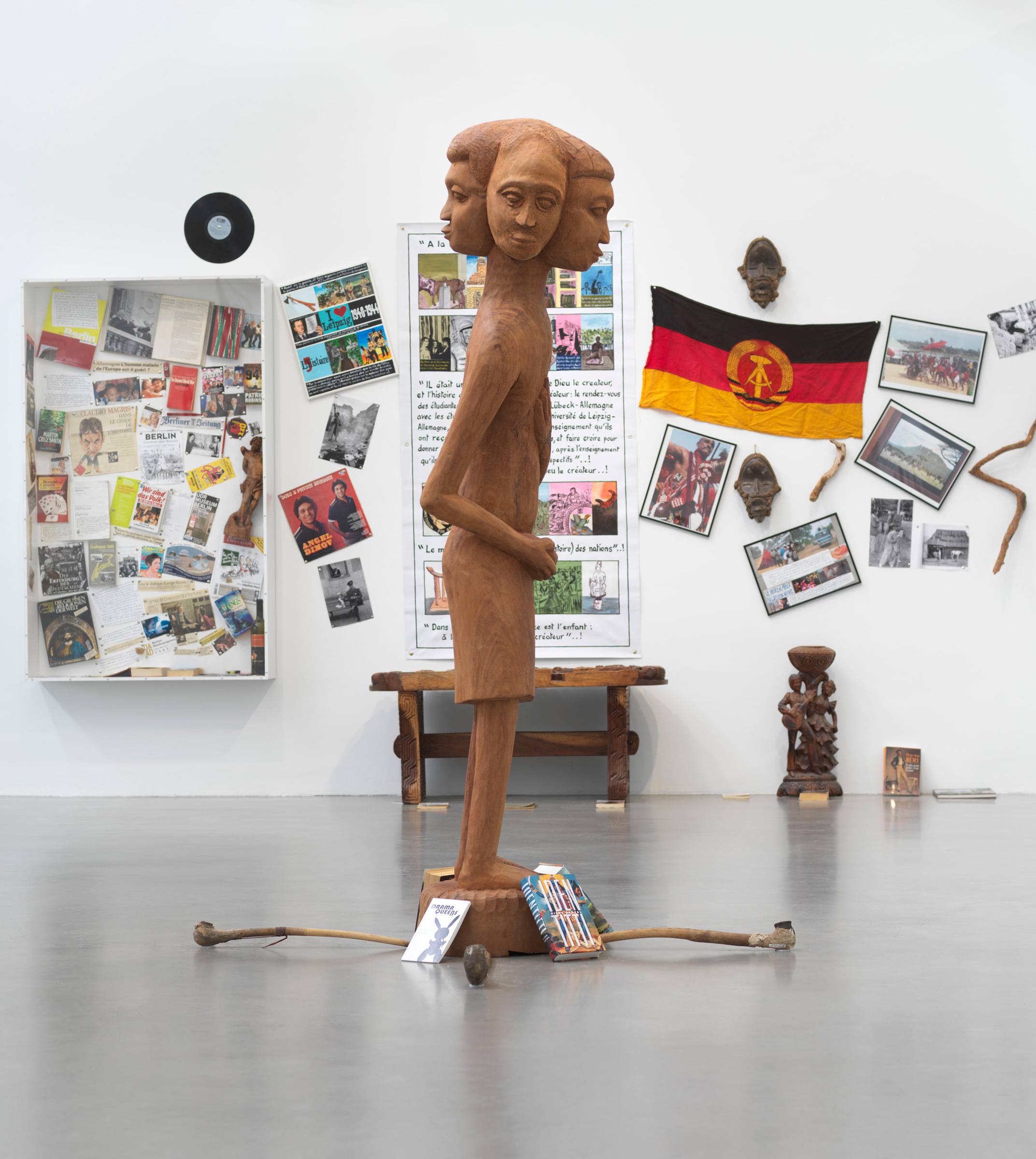 in a large space a wooden figure with four faces, in the background a flag of the GDR and a vitrine with numerous objects.