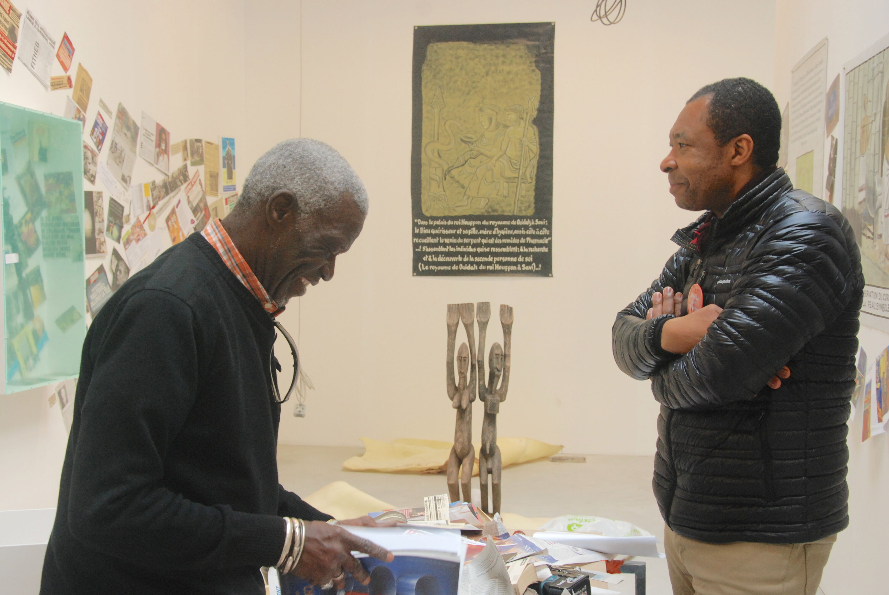 left side artist looking at a book on the table, in front of him curator Okwui Enwezor looking at him with great smile