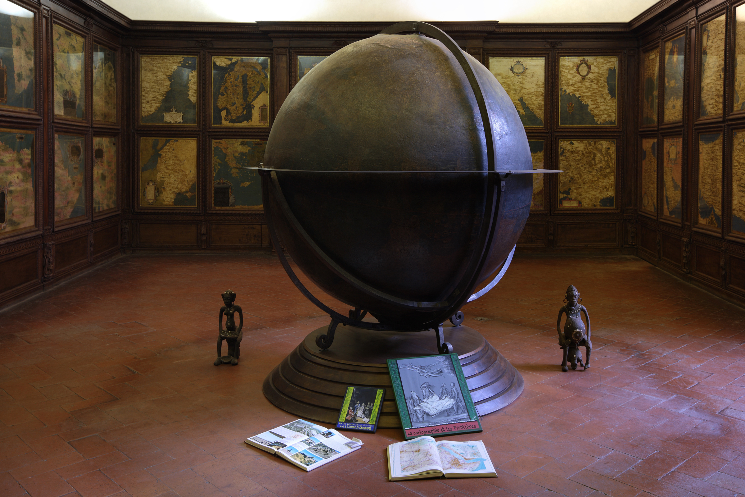 in a room with maps on the walls and a giant terrestrial globe in the center, the artist placed sculptures from Benin, paintings and books.