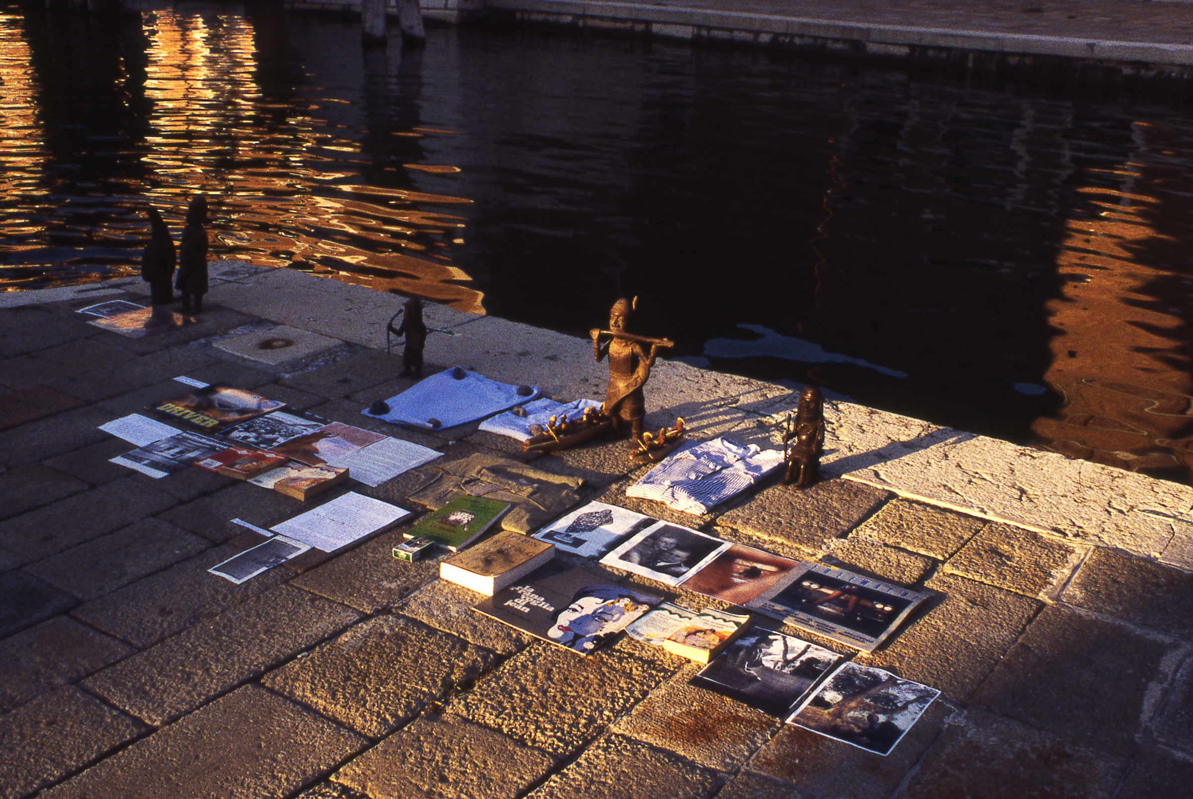an installation of books and bronze sculptures on a square in venice near a canal