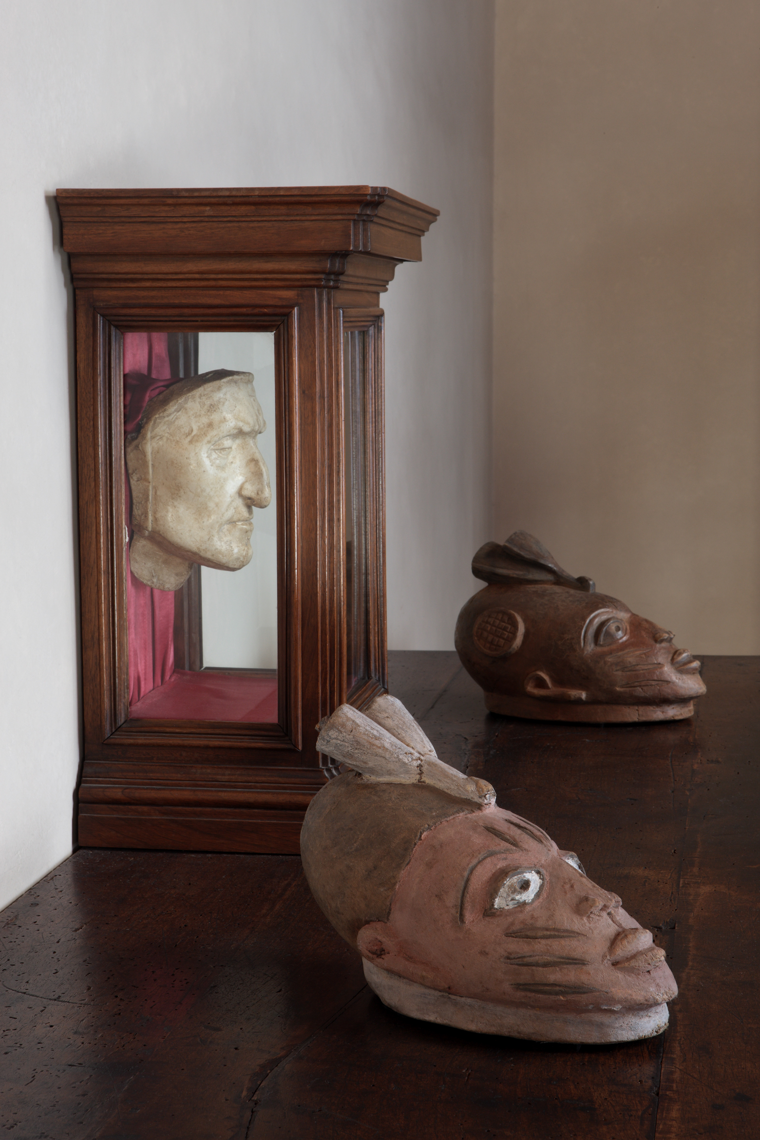 two african masks lying in front of Dante's death mask in a vitrine