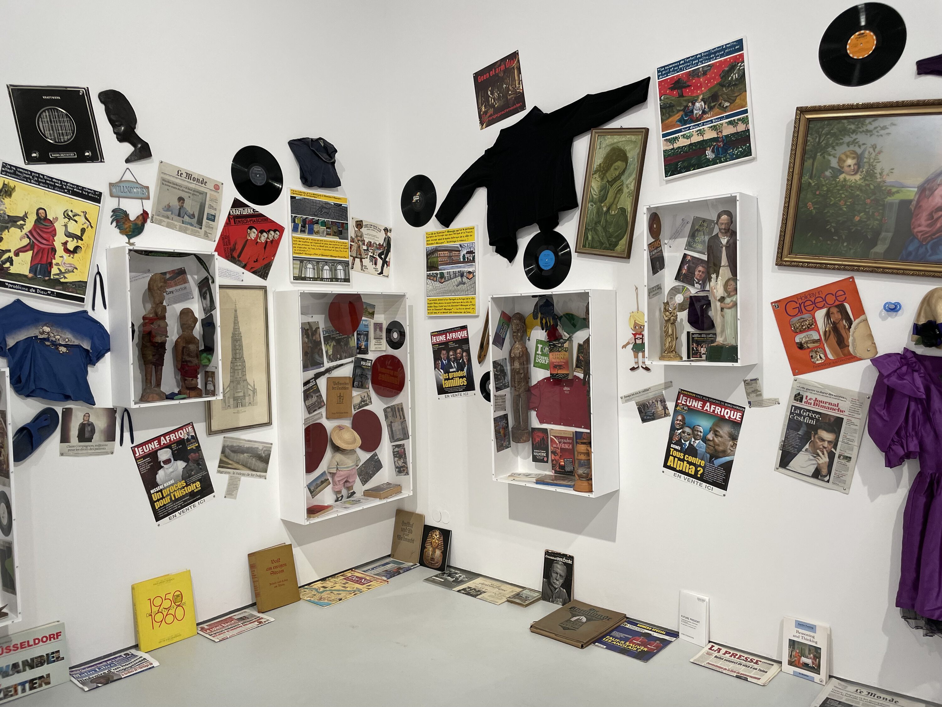 a corner of a room, on the walls textiles, records, paintings, on the floor various books