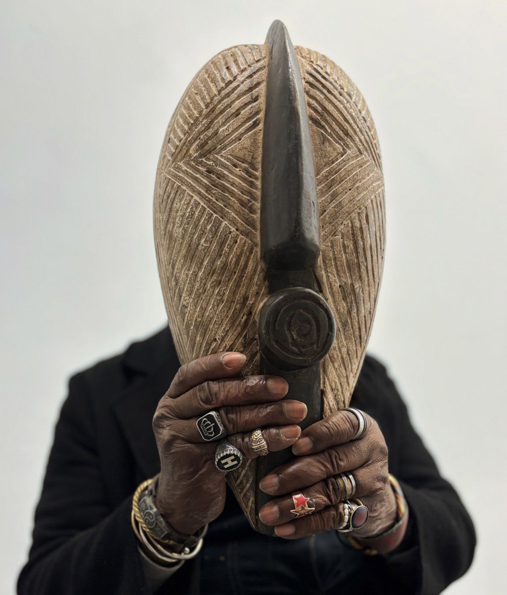 a man holds an african mask in front of his face