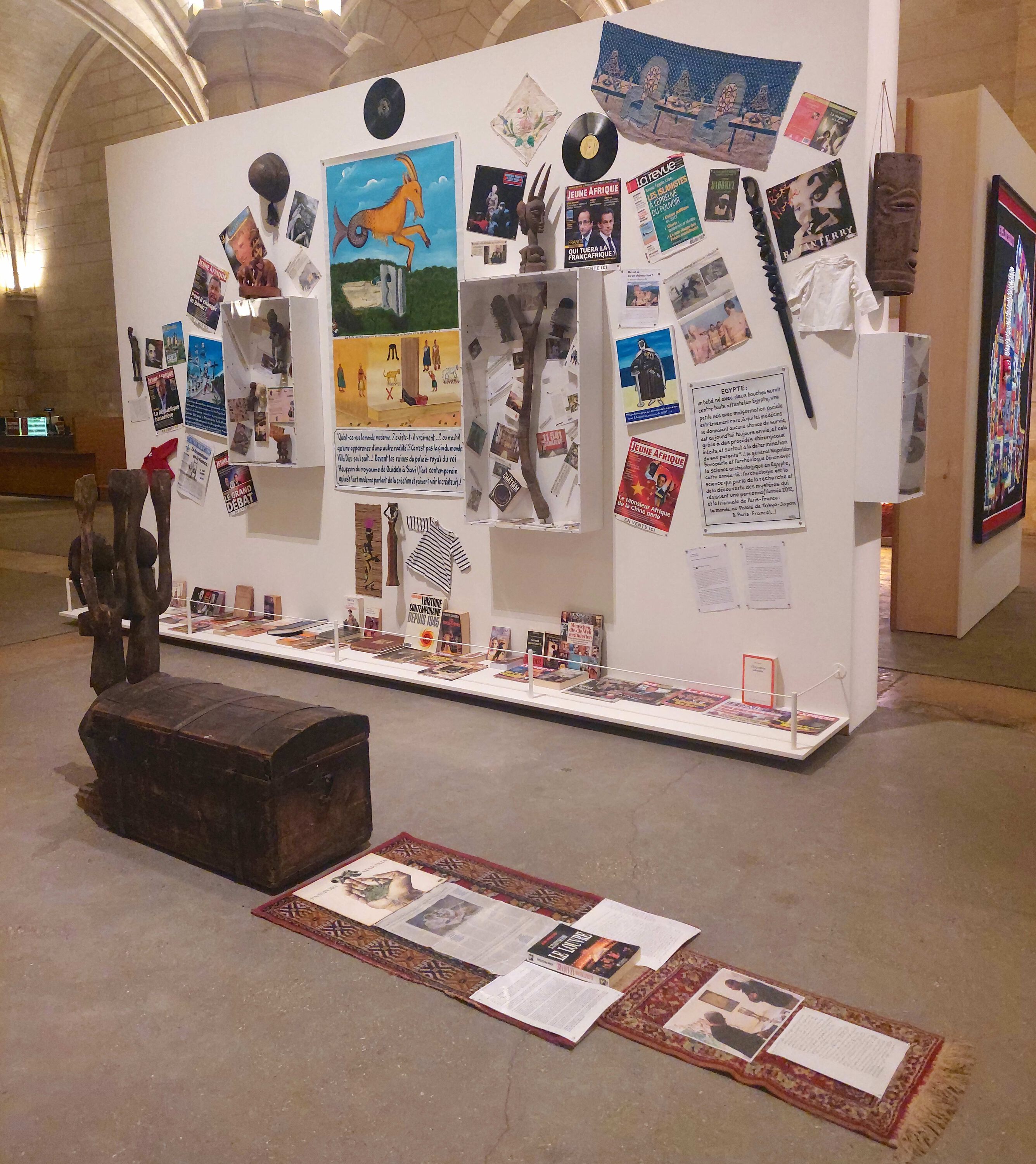 a wall covered with paintings, vinyl records and small sculptures, on a carpet photos and newsclipings