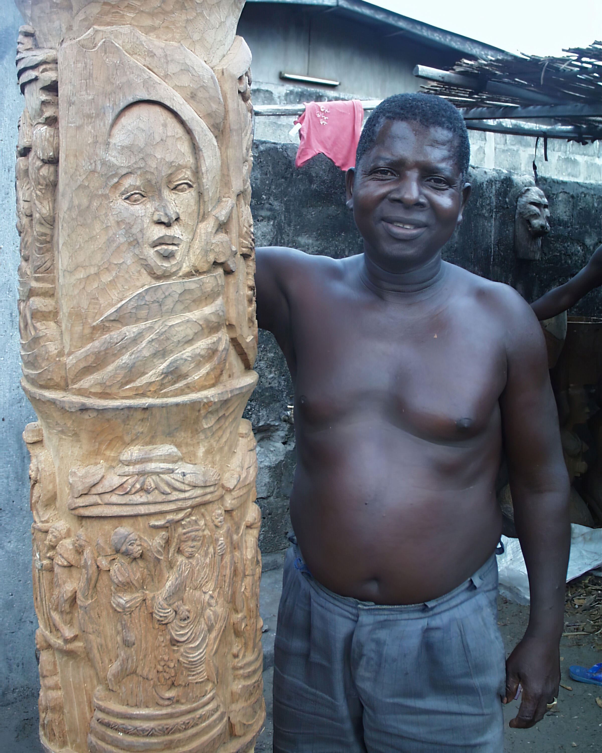 foto of finely carved wooden totem pole with artisan Edouard Kinigbè standing niext to it.