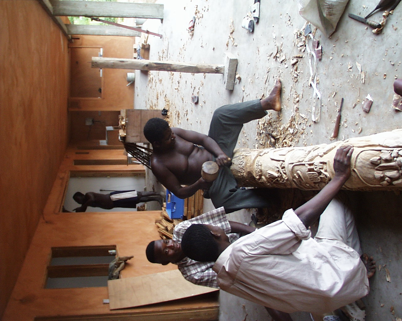 sculptor  Edouard Kinigbé works on totempole lying on the floor